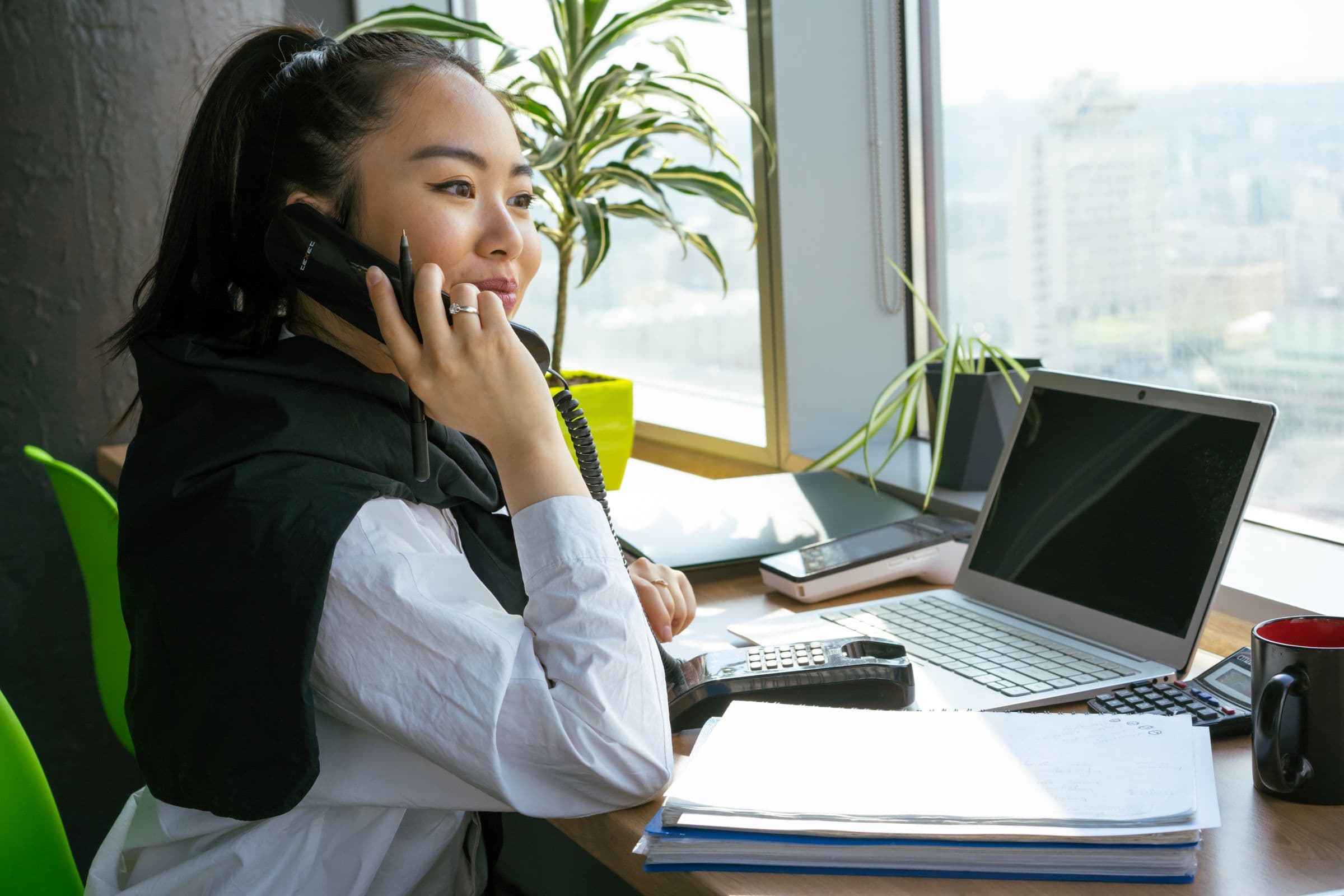 A woman taking a phone call at her desk beside a laptop